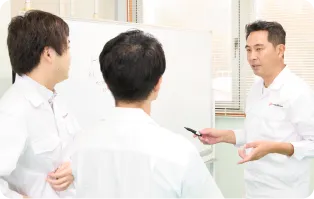 ホワイトボードの前で先輩と話し合う研究員
